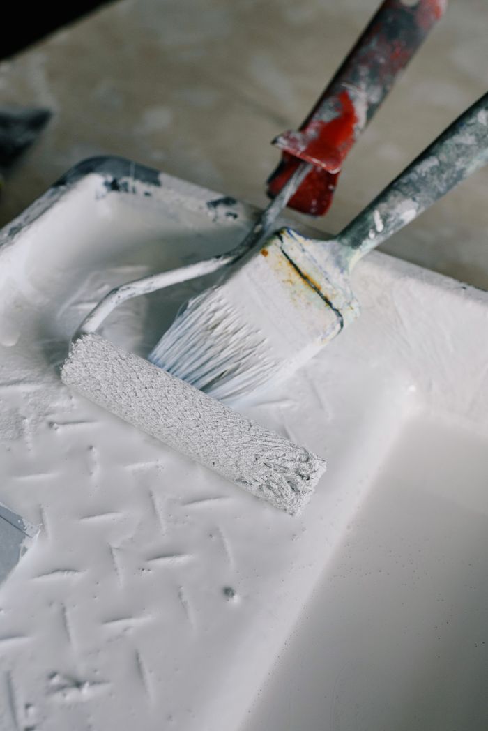 High angle wall paint roller and brush placed in paint tray with white pigment in new apartment